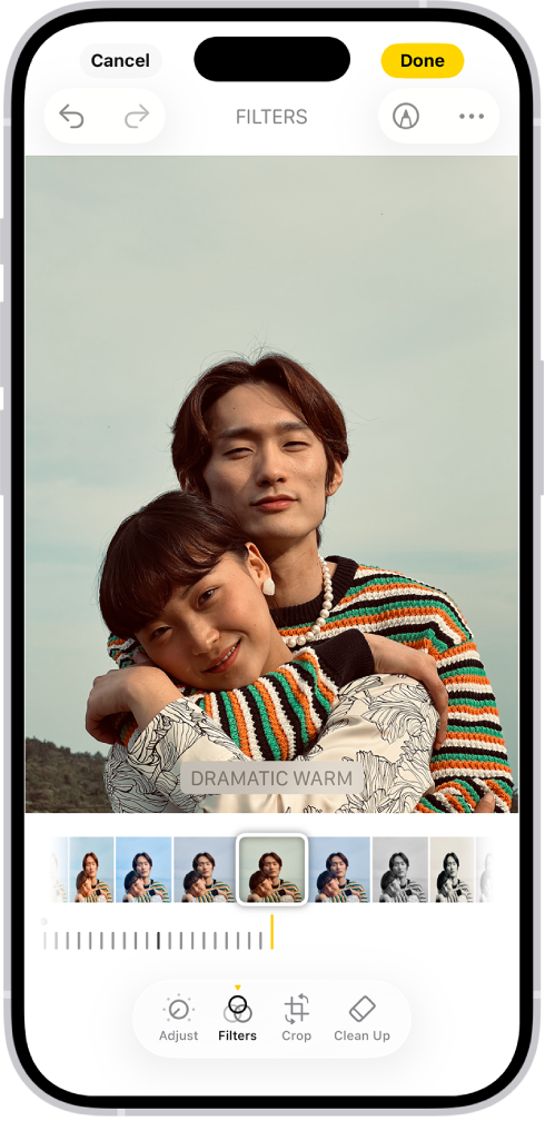 Skrin Edit dengan foto di bahagian tengah. Di bahagian bawah skrin, dari kiri ke kanan ialah butang Laraskan, Penapis, Pangkas dan Bersihkan. Butang Penapis dipilih. Di bawah foto ialah pilihan penapis berbeza. Dramatik Panas dipilih dan terdapat gelangsar untuk melaraskan keamatan penapis. Butang Batal di penjuru kiri atas skrin dan butang Selesai berada di penjuru kanan atas.