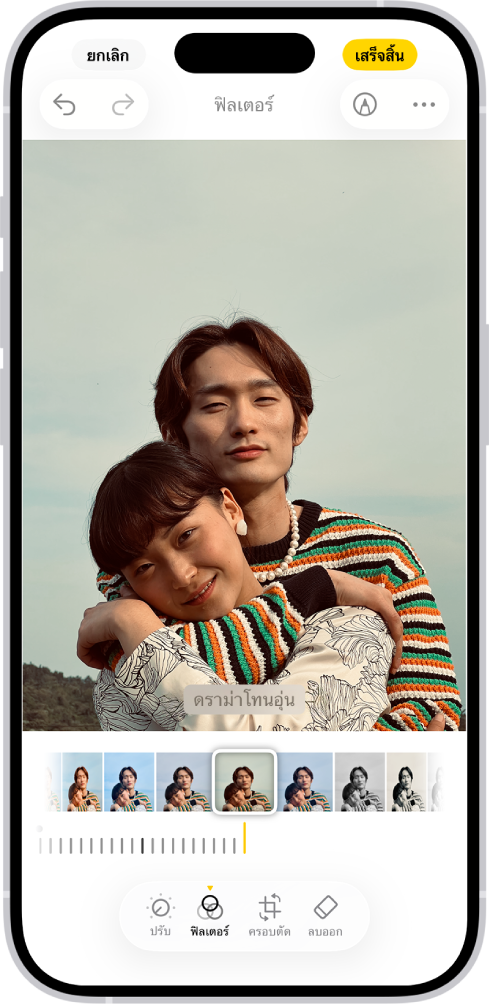 หน้าจอแก้ไขที่มีรูปภาพอยู่ตรงกลาง ด้านล่างสุดของหน้าจอโดยเรียงจากซ้ายไปขวา คือปุ่มปรับ ปุ่มฟิลเตอร์ ปุ่มครอบตัด และปุ่มลบออก ปุ่มฟิลเตอร์ถูกเลือกอยู่ ด้านล่างรูปภาพคือตัวเลือกฟิลเตอร์อื่นๆ ดราม่าโทนอุ่นถูกเลือกอยู่ และมีแถบเลื่อนเพื่อปรับความเข้มของฟิลเตอร์ ปุ่มยกเลิกอยู่ที่มุมซ้ายบนสุดของหน้าจอ และปุ่มเสร็จสิ้นอยู่ที่มุมขวาบนสุด