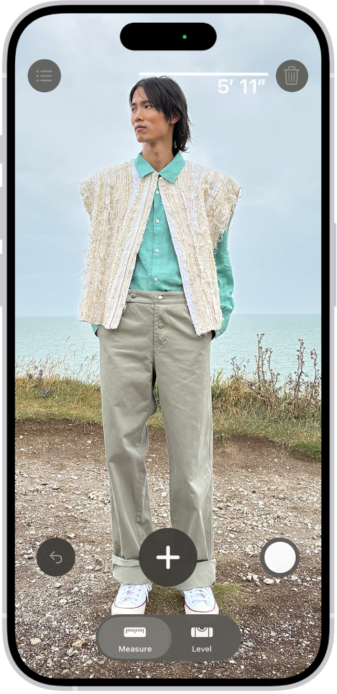 A person’s height being measured in the Measure app, with the height measurement showing at the top of the person’s head. The Take Picture button is near the lower-right corner for taking a picture of the measurement. The green Camera In Use indicator appears at the top.