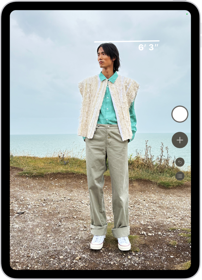 A person’s height being measured in the Measure app, with the height measurement showing at the top of the person’s head. The Take Picture button is near the lower-right corner for taking a picture of the measurement. The green Camera In Use indicator appears at the top.