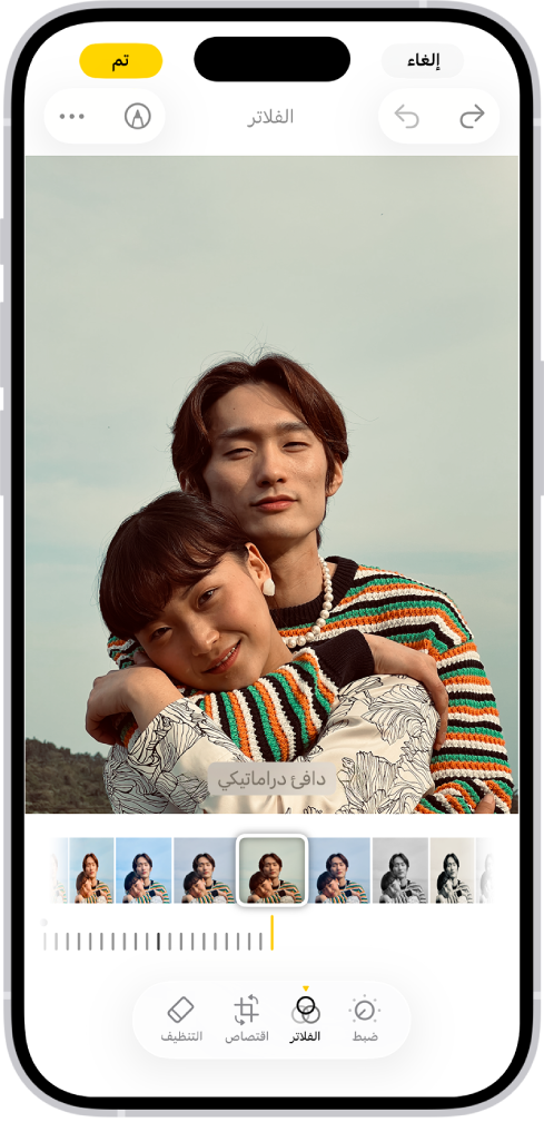 شاشة تعديل مع عرض صورة في المنتصف. في الجزء السفلي من الشاشة، من اليمين إلى اليسار، تظهر أزرار ضبط والفلاتر واقتصاص وتنظيف. زر الفلاتر محدد. أسفل الصورة توجد خيارات الفلترة المختلفة. خيار "دافئ دراماتيكي" محدد ويوجد شريط تمرير لضبط شدة الفلتر. زر الإلغاء يظهر في الزاوية العلوية اليمنى من الشاشة، ويظهر زر تم في الزاوية العلوية اليسرى.