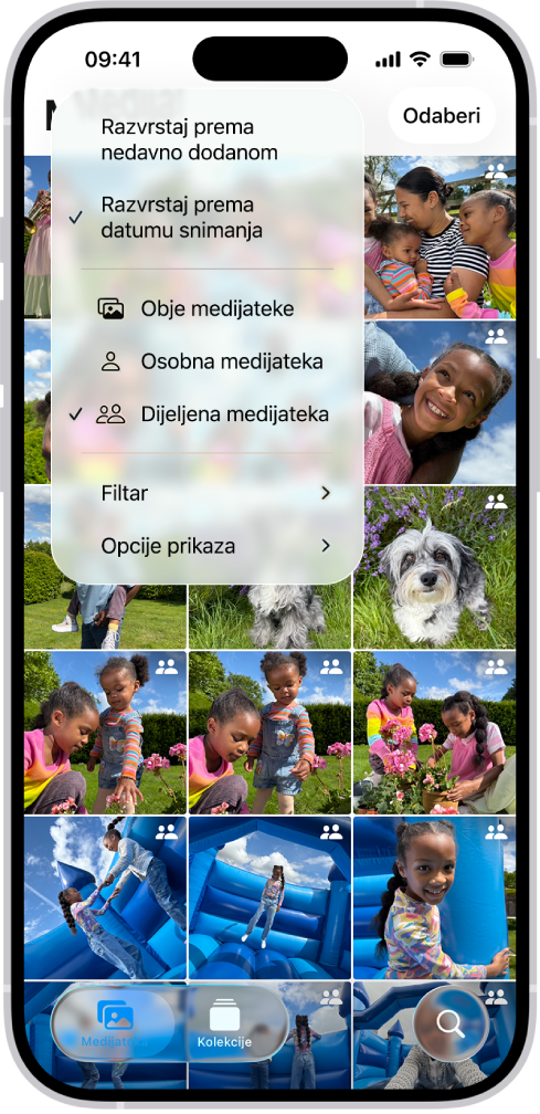 iCloud dijeljena medijateka fotografija u aplikaciji Foto. Odabrana je tipka Dijeljena medijateka u donjem lijevom kutu i odabrana je Dijeljena medijateka na popisu opcija medijateke. Sve fotografije prikazane u medijateci imaju bedž dijeljene medijateke u gornjem desnom kutu.