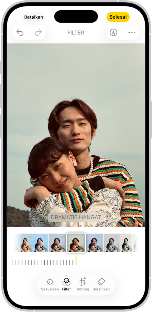 Layar Edit dengan foto di tengah. Di bagian bawah layar, dari kiri ke kanan, terdapat tombol Sesuaikan, Filter, Potong, dan Bersihkan. Tombol Filter dipilih. Di bawah foto terdapat berbagai pilihan filter. Hangat Dramatis dipilih dan terdapat penggeser untuk menyesuaikan intensitas filter. Tombol Batalkan terdapat di pojok kiri atas layar dan tombol Selesai terdapat di pojok kanan atas.