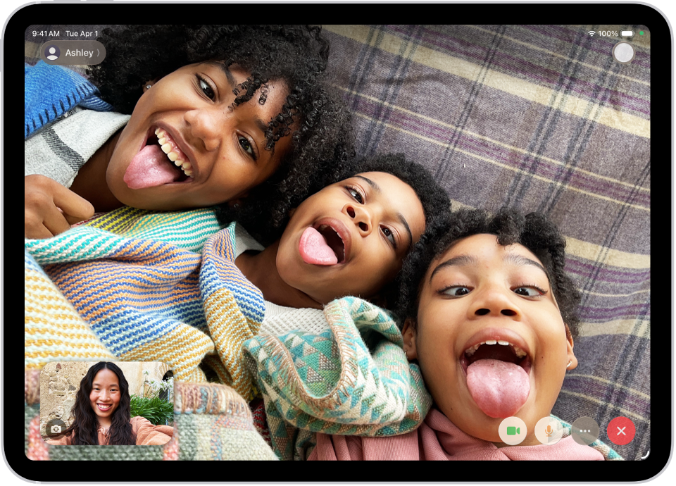 Notiek FaceTime video zvans, kura apakšējā daļā ir redzams viens dalībnieks. Trīs citu dalībnieku attēls aizpilda pārējo ekrāna daļu. Apakšējā labajā stūrī ir pogas Camera, Microphone, More un End Call.