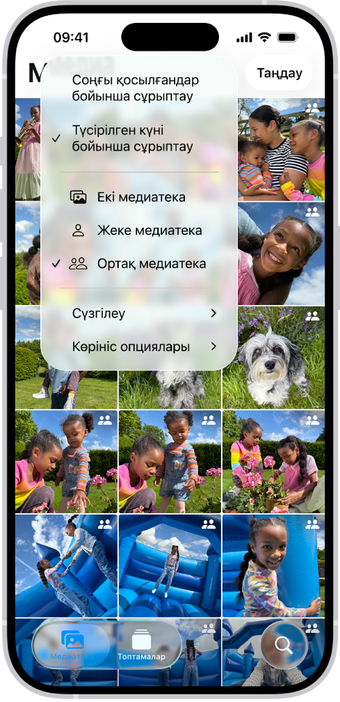 «Фотолар» қолданбасындағы iCloud ортақ фотолар жинағы. Төменгі сол жақ бұрышта «Ортақ медиатека» түймесі таңдалған және медиатека опцияларын тізімінен «Ортақ медиатека» таңдалған. Медиатекада көрсетілген барлық фотода жоғарғы оң жақ бұрышында ортақ медиатека белгісі бар.